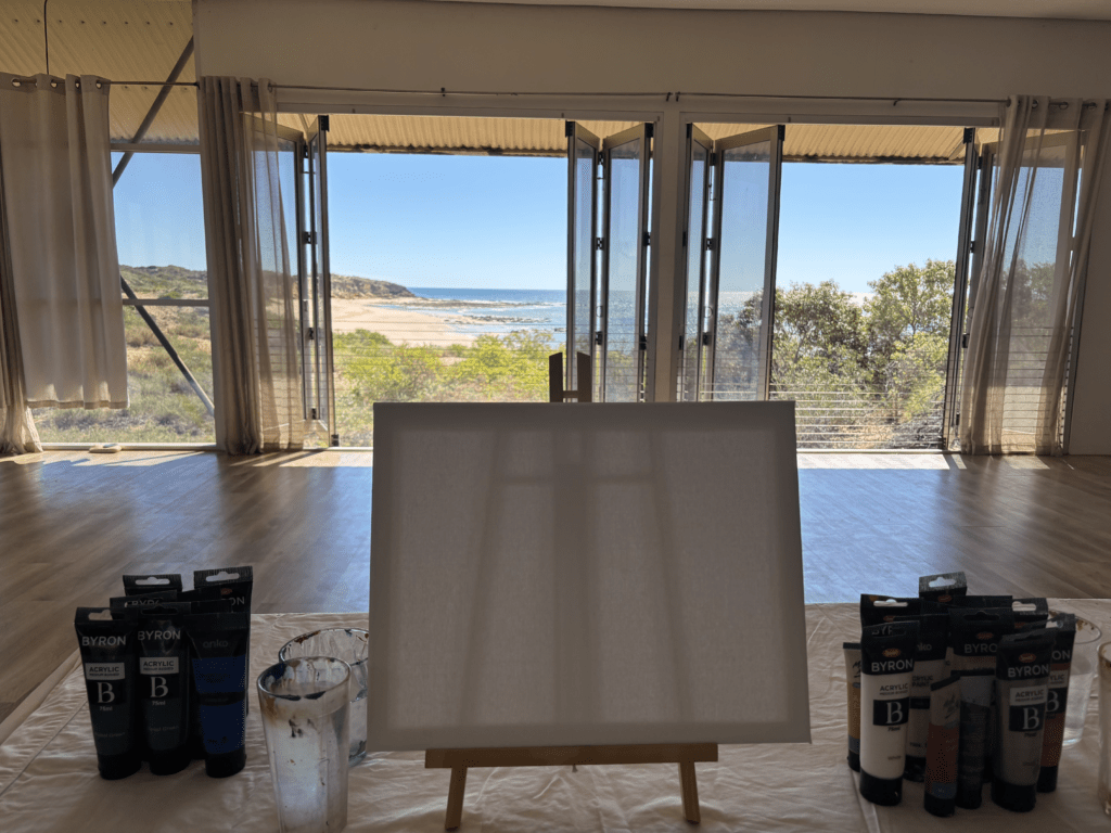 Blank canvas on an easel overlooking the Kimberley coastline, surrounded by acrylic paints and brushes, symbolizing creativity, mindfulness, and intentional rest.
