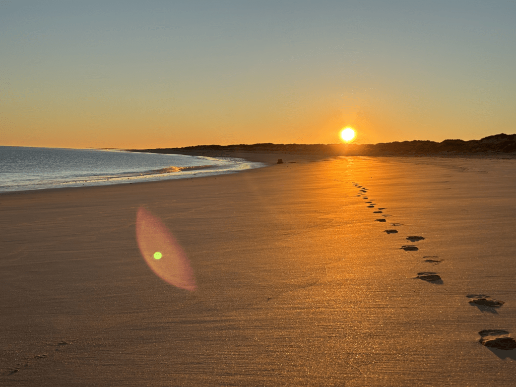Footprints leading along an empty beach at sunrise, representing mindful walking and intentional rest.